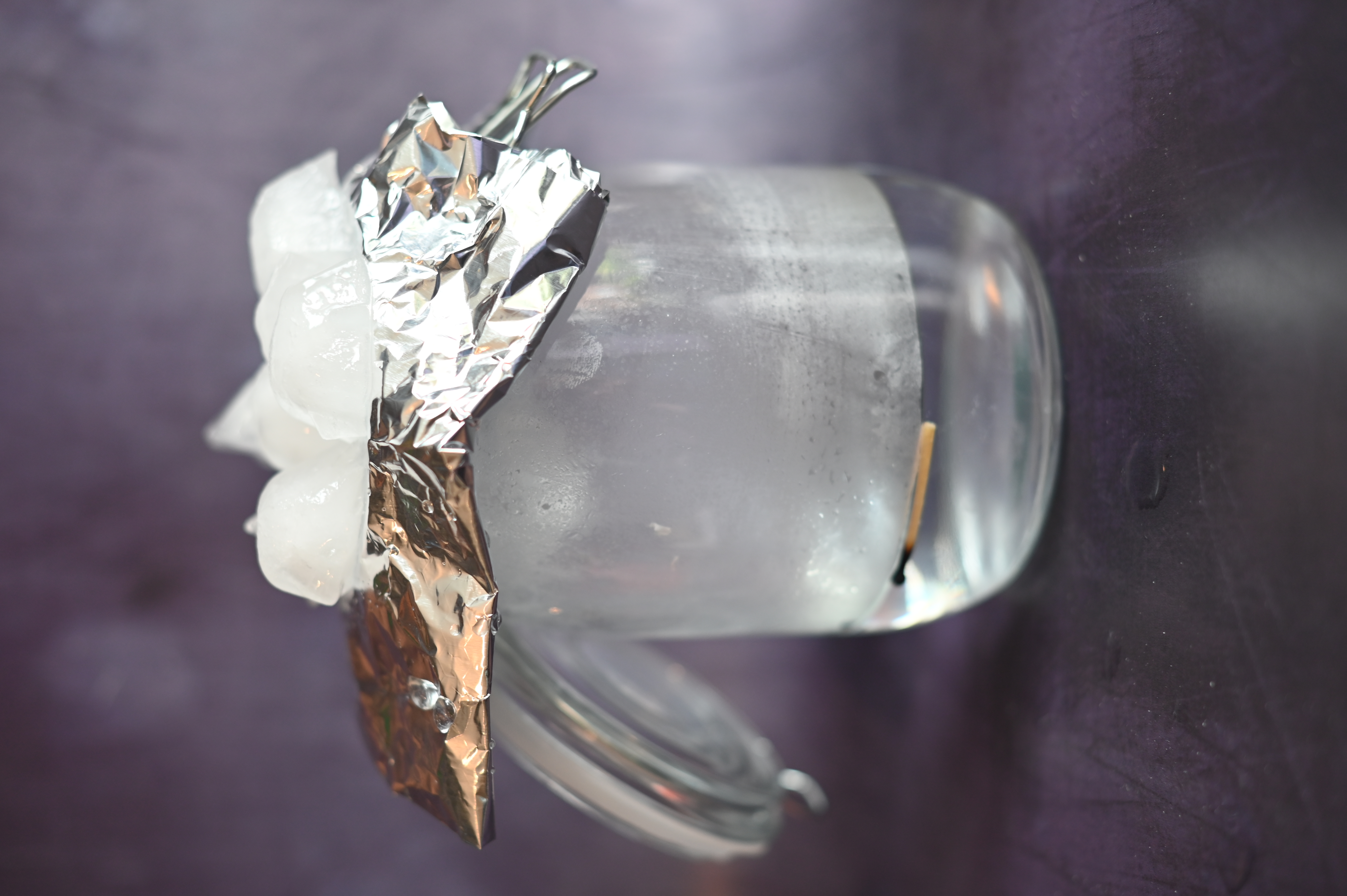 A glass jar, one quarter full of warm water  with foil and ice on top