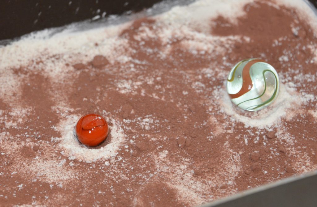 Two marbles sitting in a tray of flour and hot chocolate to demonstrate how craters form